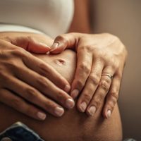 Detail of woman's both hands placed on her pregnant belly.
